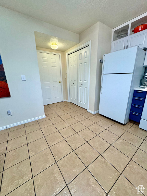 Kitchen featuring light tile floors, white cabinetry, and white fridge