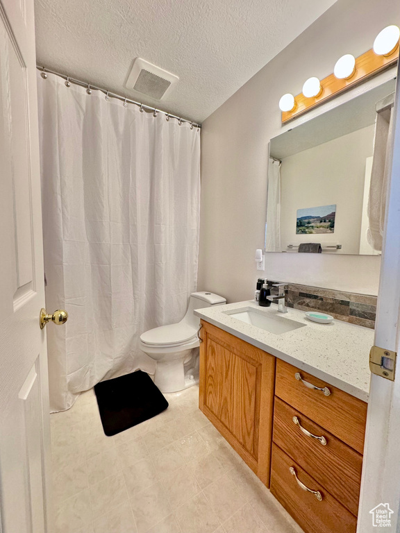 Bathroom featuring toilet, a textured ceiling, vanity, and tile flooring