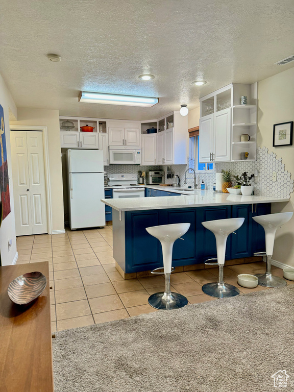 Kitchen featuring kitchen peninsula, white appliances, light tile floors, white cabinets, and a breakfast bar area