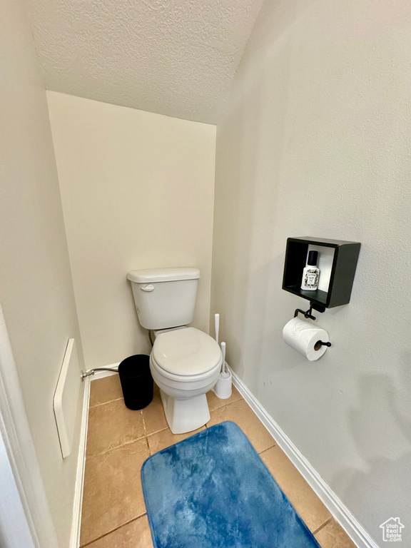 Bathroom with toilet, a textured ceiling, and tile floors