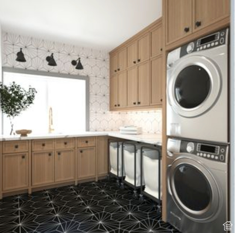 Clothes washing area with a healthy amount of sunlight, stacked washer / dryer, dark tile floors, and sink
