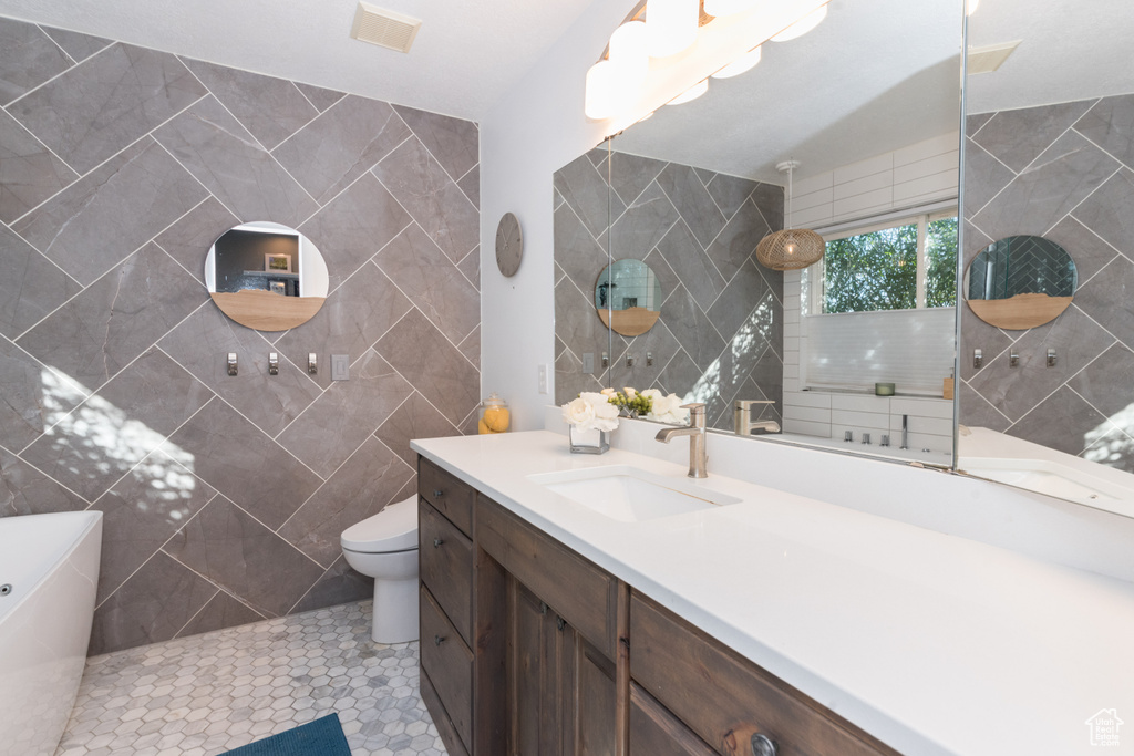 Bathroom featuring tile walls, toilet, vanity with extensive cabinet space, and tile flooring