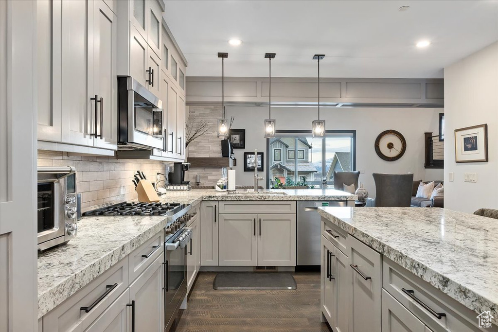 Kitchen with dark hardwood / wood-style floors, pendant lighting, light stone counters, appliances with stainless steel finishes, and tasteful backsplash