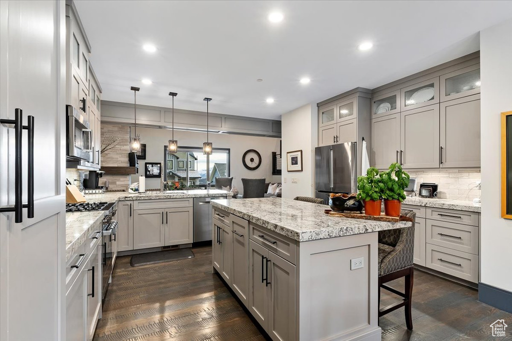 Kitchen with dark hardwood / wood-style floors, kitchen peninsula, a breakfast bar, backsplash, and stainless steel appliances