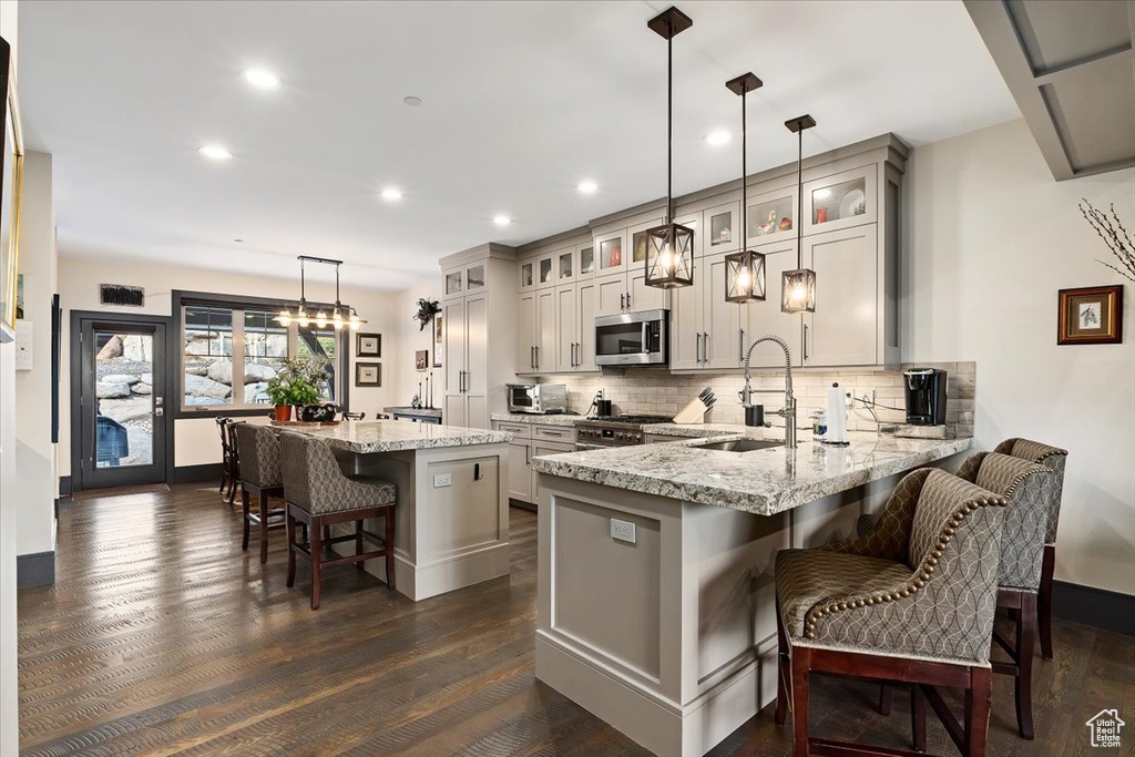 Kitchen featuring a kitchen bar, pendant lighting, appliances with stainless steel finishes, and dark hardwood / wood-style flooring