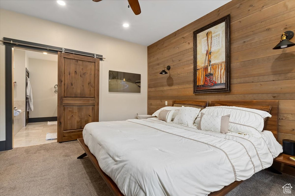 Bedroom with light carpet, wooden walls, a barn door, and ceiling fan