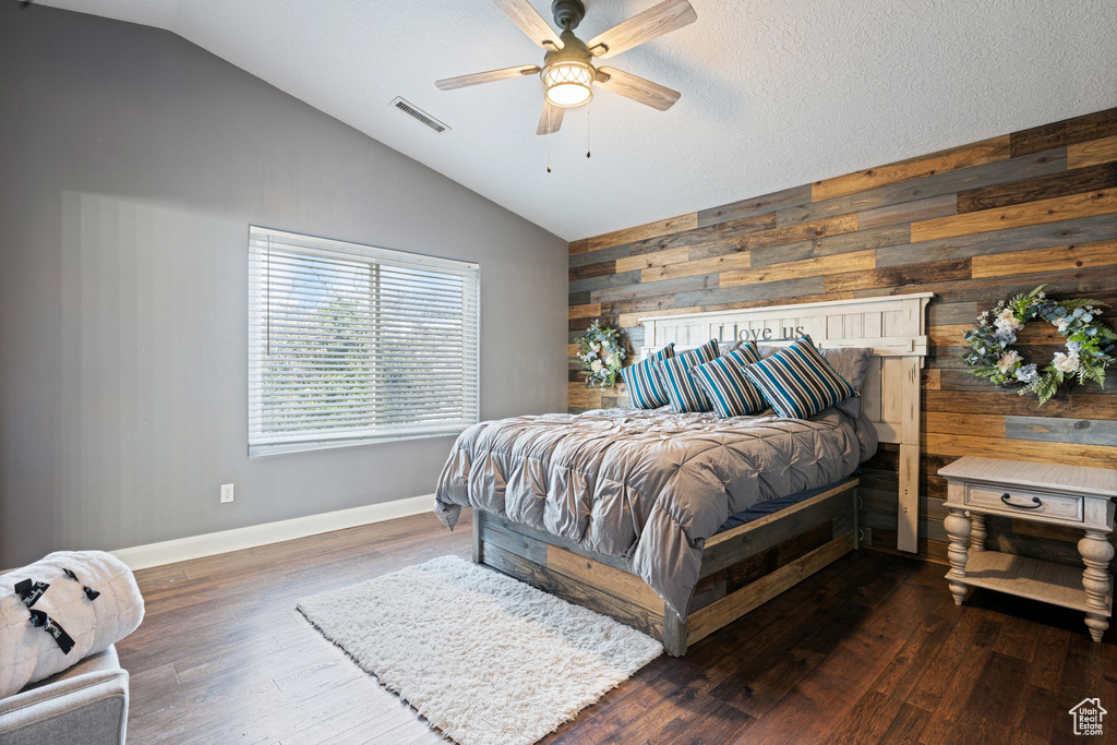 Bedroom featuring lofted ceiling, wood walls, ceiling fan, and dark wood-type flooring