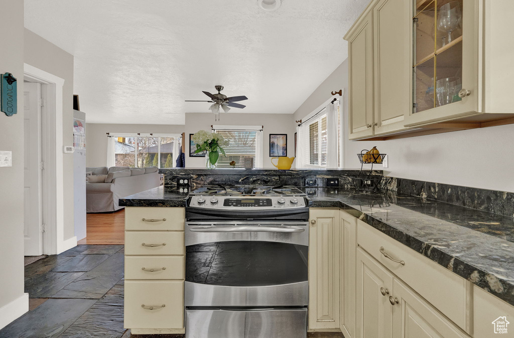 Kitchen with kitchen peninsula, ceiling fan, dark tile flooring, cream cabinetry, and stainless steel stove