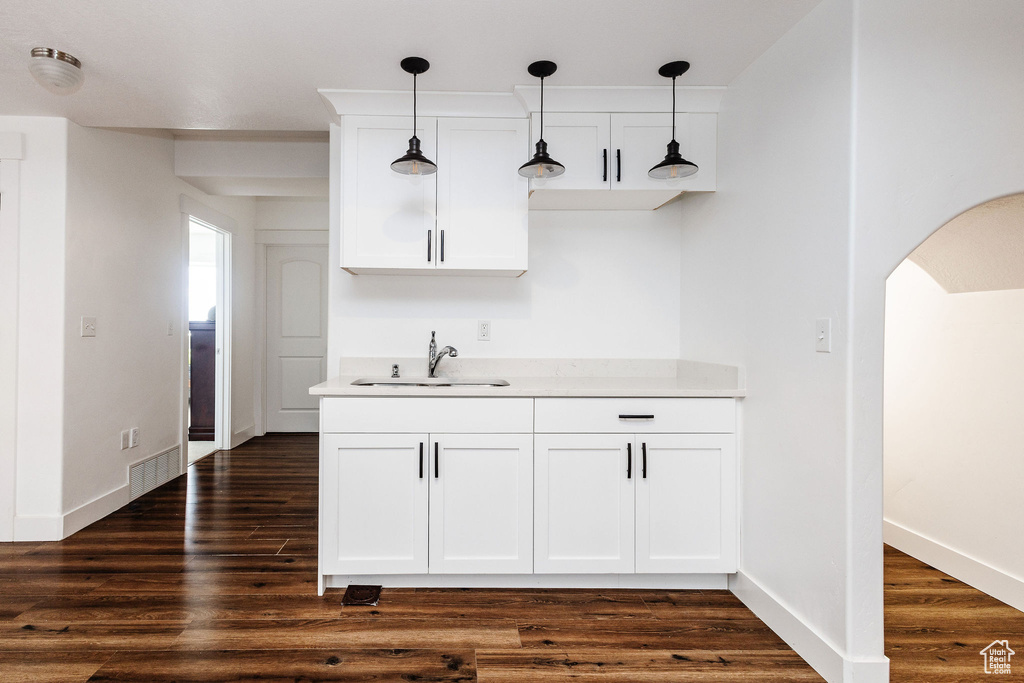 Bar with hanging light fixtures, dark wood-type flooring, white cabinetry, and sink