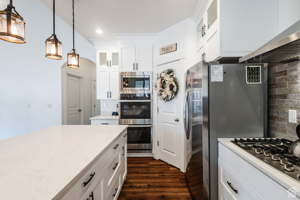 Kitchen featuring hanging light fixtures, dark hardwood / wood-style flooring, white cabinets, backsplash, and stainless steel appliances