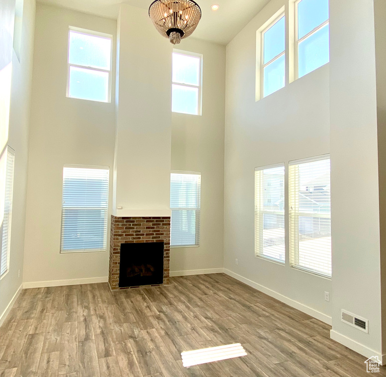 Unfurnished living room featuring plenty of natural light, a brick fireplace, light hardwood / wood-style flooring, and a towering ceiling
