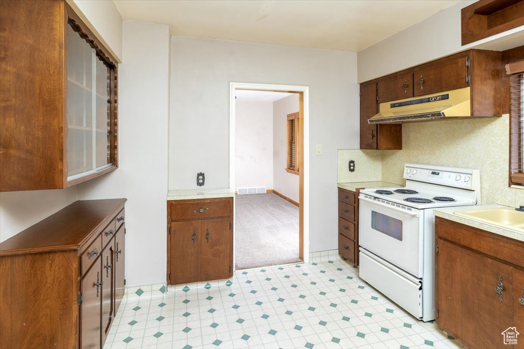 Kitchen with electric stove, sink, light tile floors, premium range hood, and tasteful backsplash