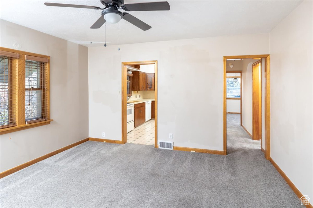 Unfurnished bedroom featuring light carpet, ensuite bathroom, and ceiling fan