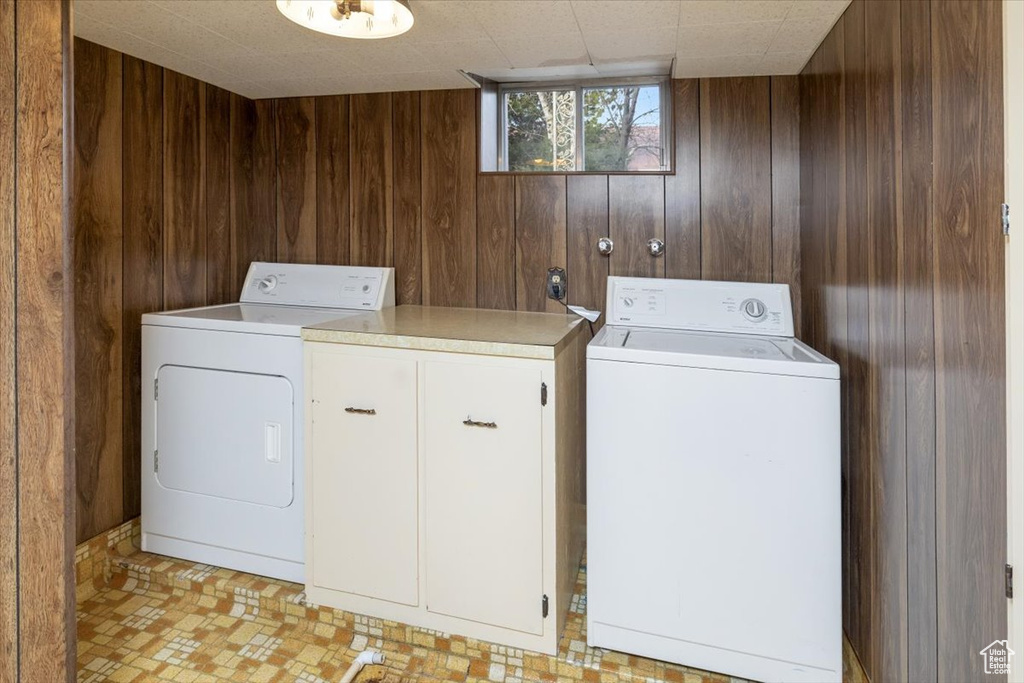 Laundry room featuring wood walls, cabinets, washing machine and clothes dryer, and light tile flooring