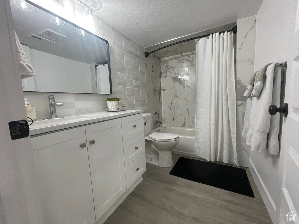 Full bathroom featuring vanity, hardwood / wood-style floors, a textured ceiling, toilet, and shower / tub combo