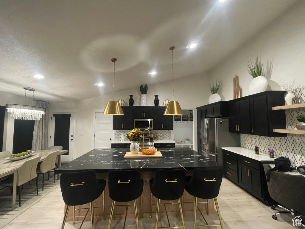 Kitchen with backsplash, a center island with sink, stainless steel appliances, and pendant lighting