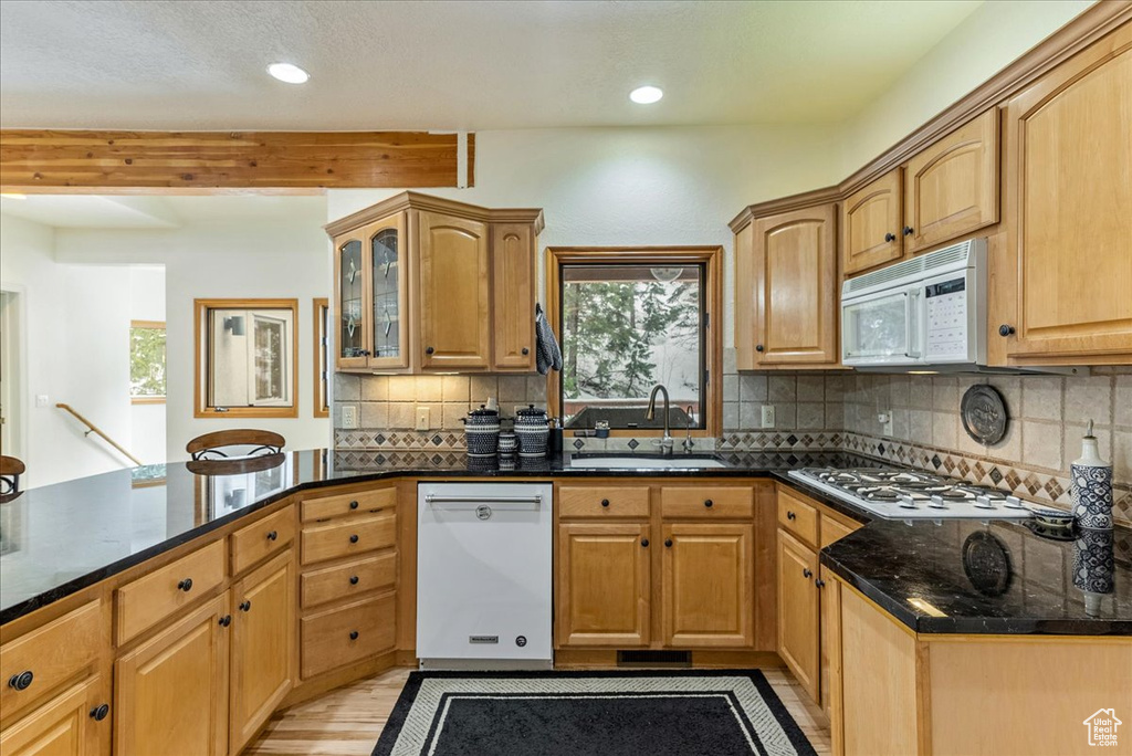 Kitchen with dark stone counters, tasteful backsplash, light hardwood / wood-style flooring, white appliances, and sink