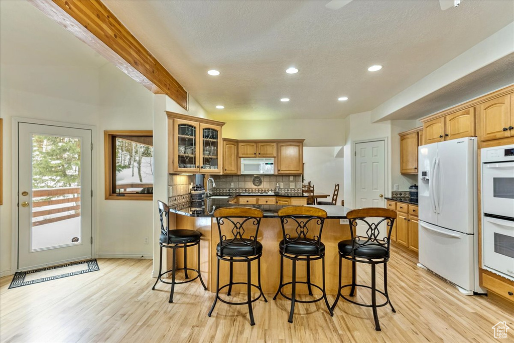 Kitchen with backsplash, beamed ceiling, white appliances, light wood-type flooring, and a breakfast bar area