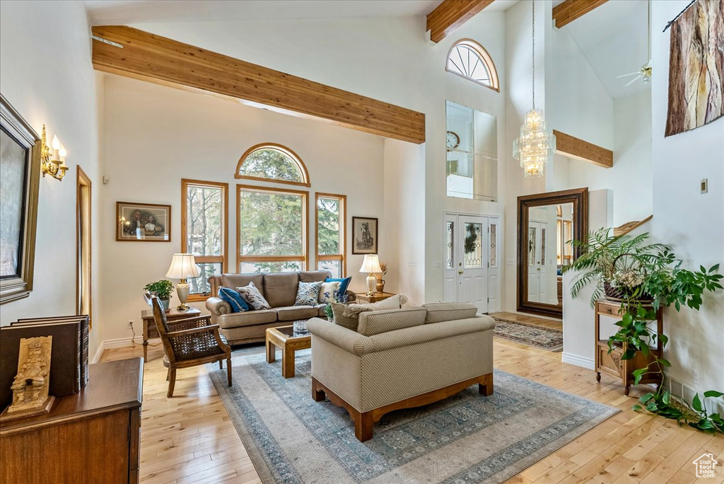Living room with beam ceiling, high vaulted ceiling, light hardwood / wood-style floors, and ceiling fan with notable chandelier