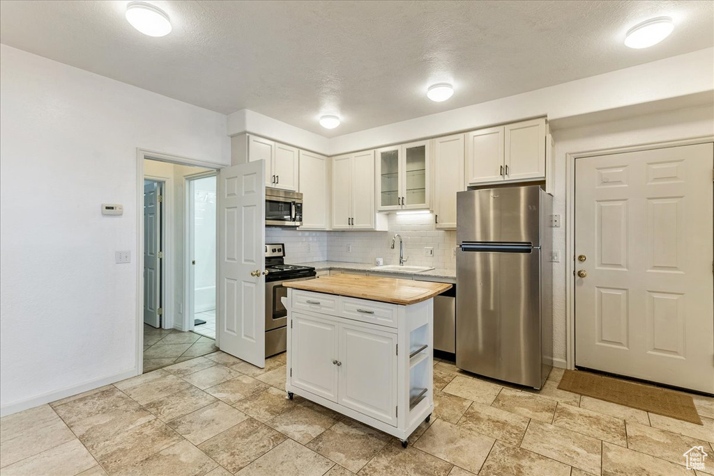 Kitchen with light tile flooring, wooden counters, white cabinets, and stainless steel appliances