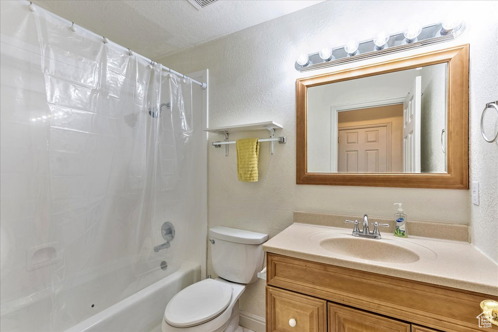 Full bathroom with toilet, a textured ceiling, vanity, and shower / bath combo with shower curtain