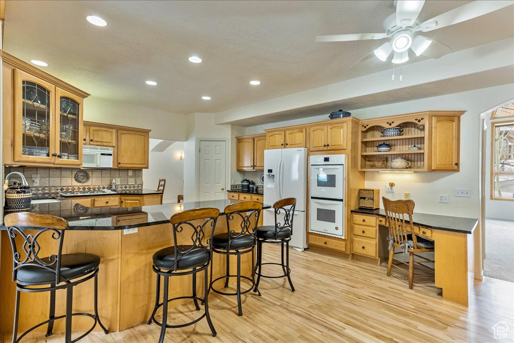 Kitchen with ceiling fan, a kitchen breakfast bar, white appliances, and light wood-type flooring