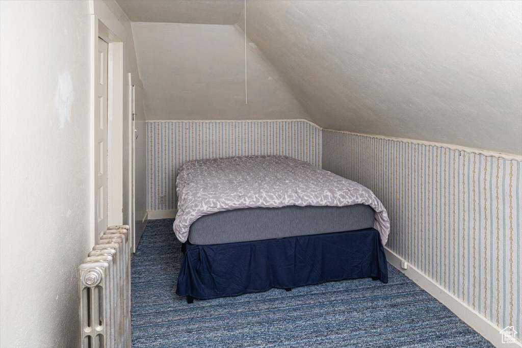 Bedroom with vaulted ceiling, radiator, and dark colored carpet