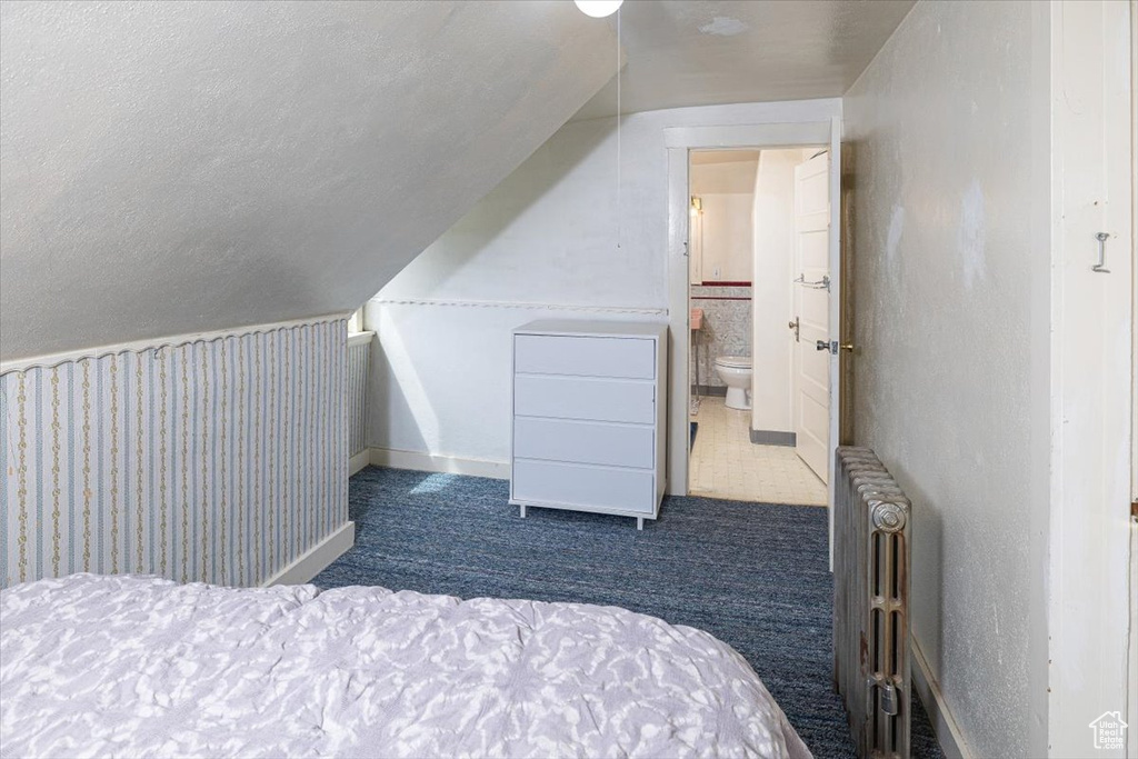 Carpeted bedroom with connected bathroom, a textured ceiling, vaulted ceiling, and radiator heating unit