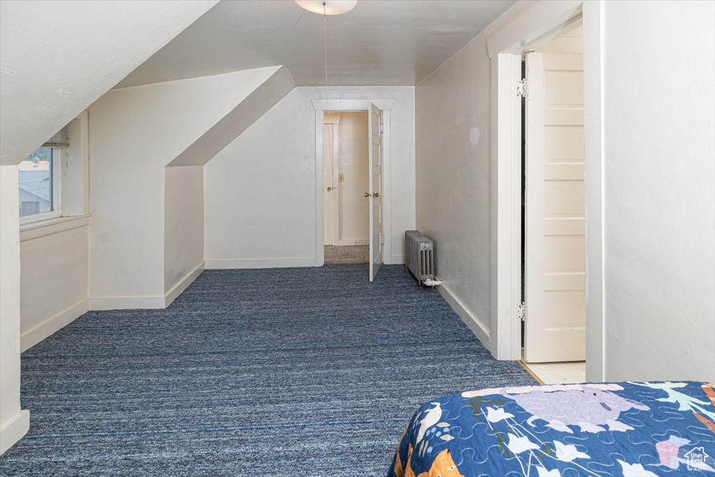 Bonus room with dark colored carpet and radiator heating unit