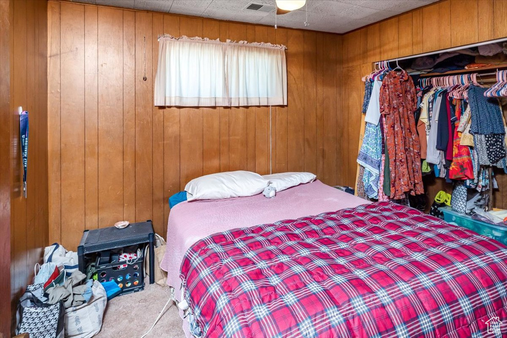 Bedroom featuring light carpet, wooden walls, and a closet