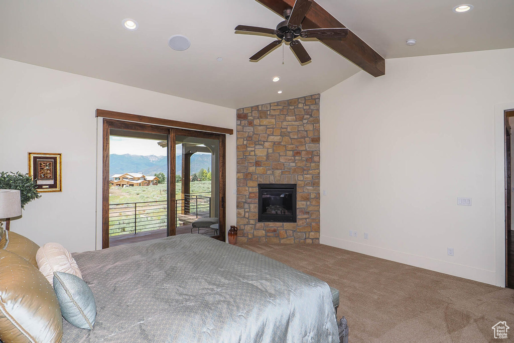 Carpeted bedroom featuring vaulted ceiling with beams, ceiling fan, a stone fireplace, and access to outside