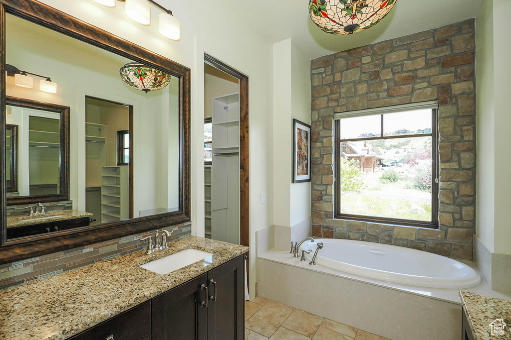Bathroom featuring tasteful backsplash, a washtub, vanity with extensive cabinet space, and tile flooring