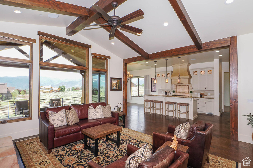 Living room with vaulted ceiling with beams, dark hardwood / wood-style floors, and ceiling fan with notable chandelier