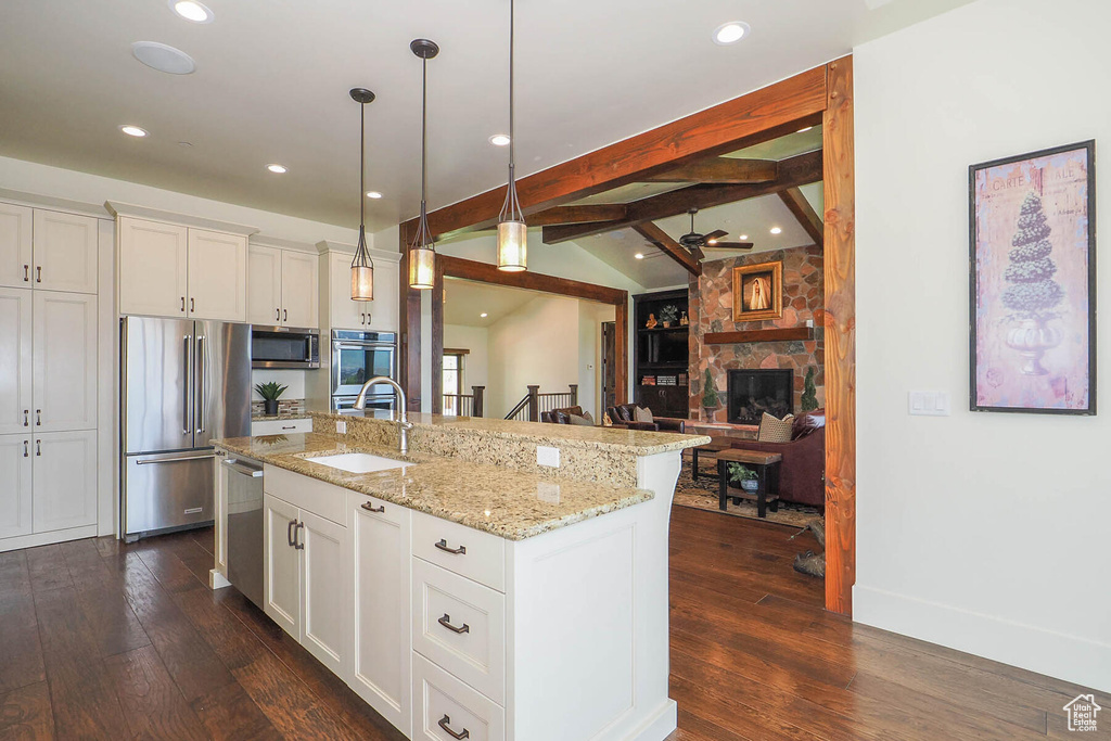 Kitchen featuring a kitchen island with sink, appliances with stainless steel finishes, dark wood-type flooring, and a fireplace