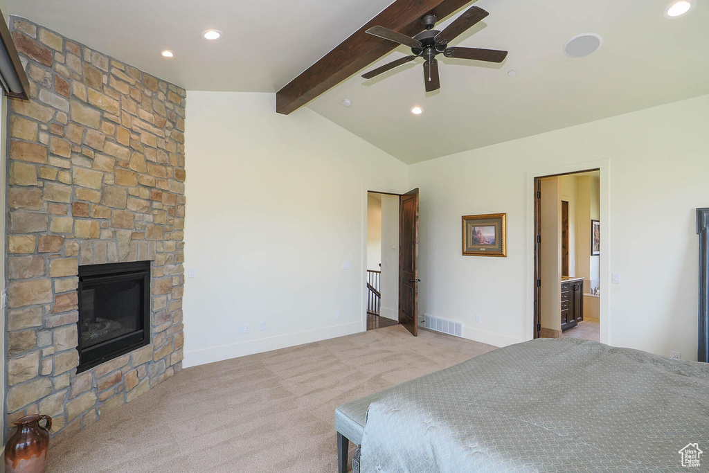 Carpeted bedroom with ensuite bathroom, a fireplace, ceiling fan, and vaulted ceiling with beams