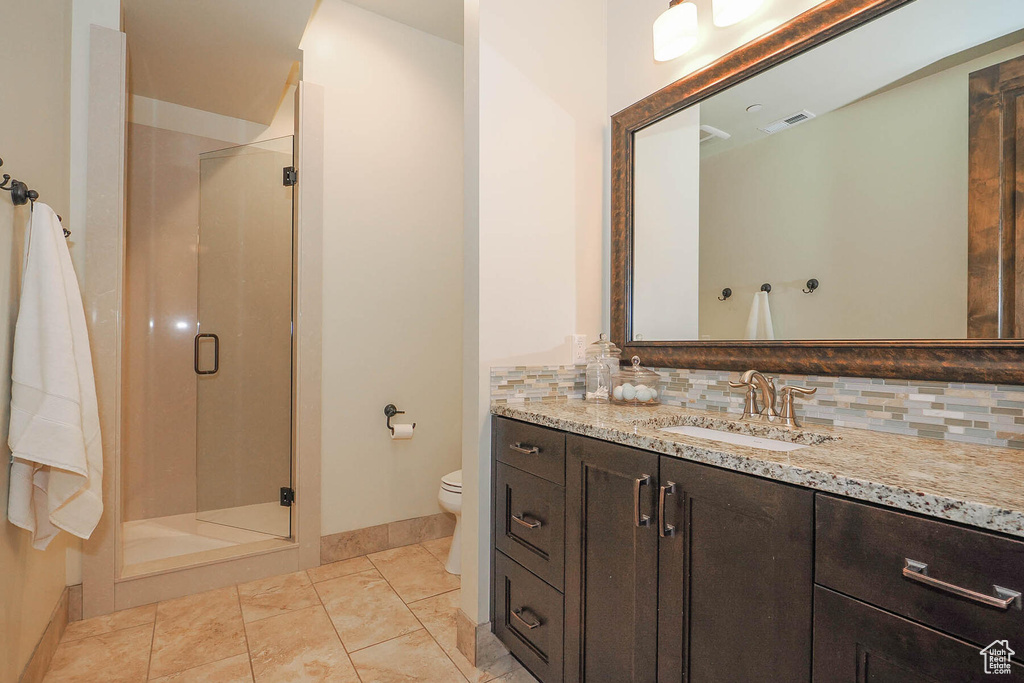 Bathroom featuring toilet, a shower with door, backsplash, tile flooring, and large vanity
