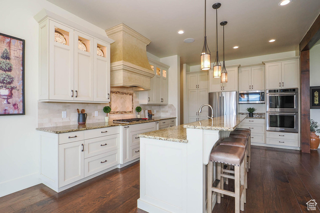 Kitchen featuring a kitchen breakfast bar, backsplash, a center island with sink, stainless steel appliances, and premium range hood