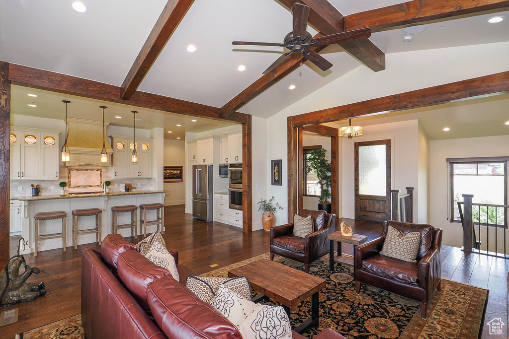 Living room with dark wood-type flooring, vaulted ceiling with beams, and ceiling fan with notable chandelier