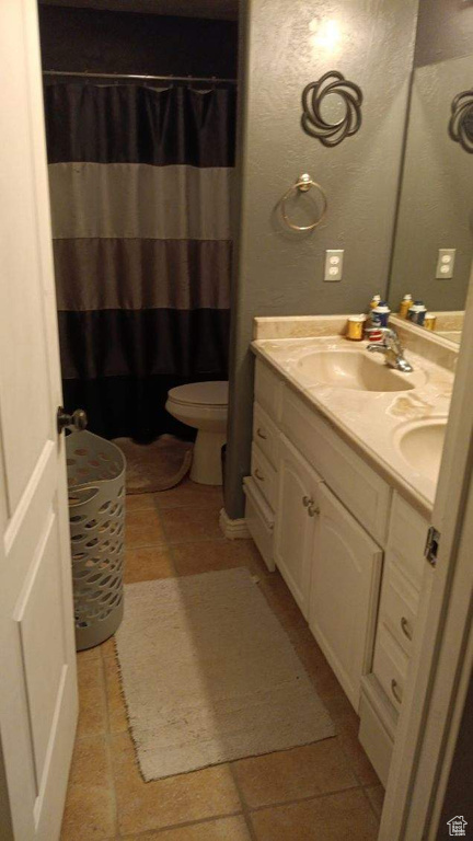Bathroom featuring dual bowl vanity, toilet, and tile floors