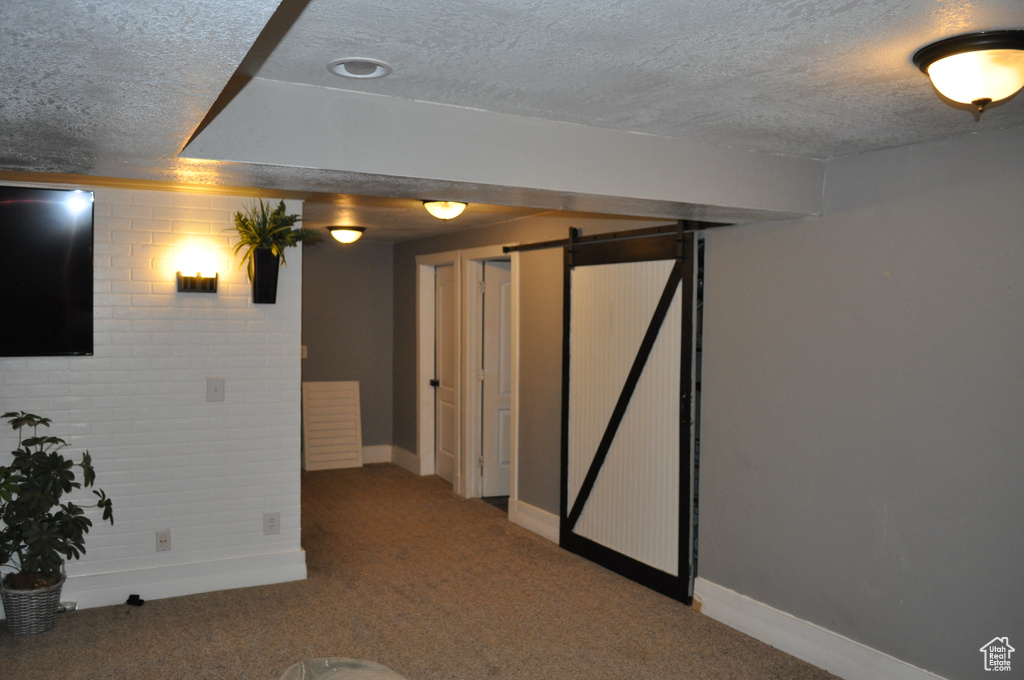 Basement with a barn door, carpet floors, brick wall, and a textured ceiling