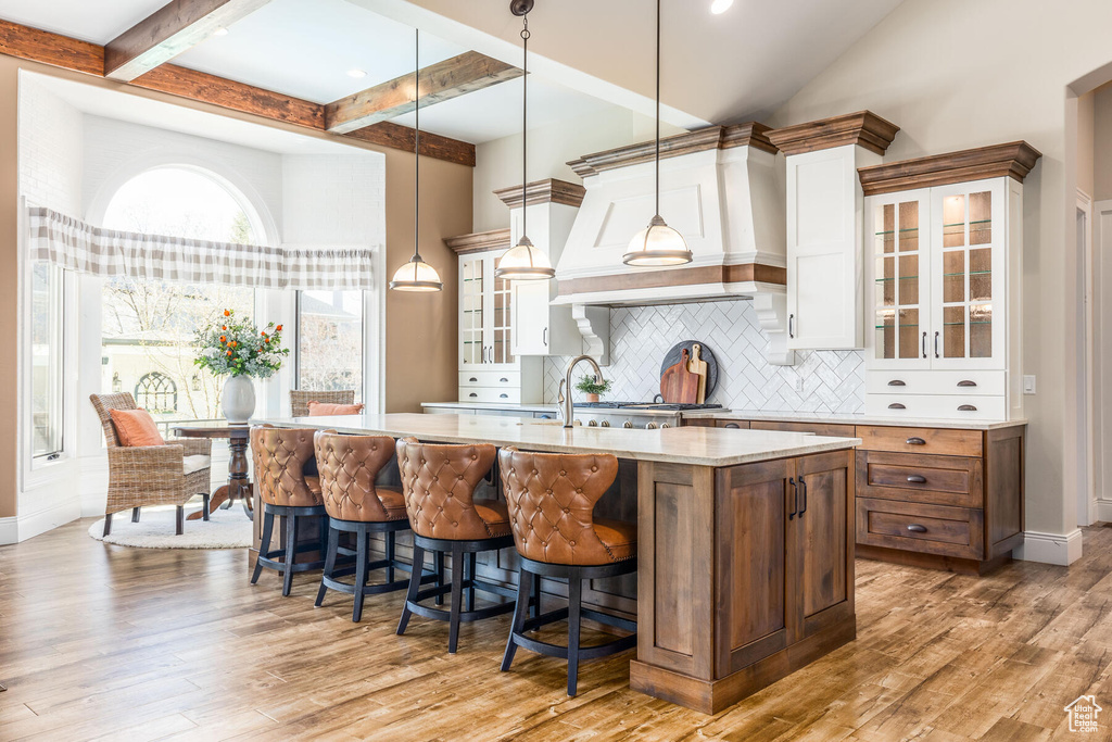 Kitchen featuring premium range hood, decorative light fixtures, tasteful backsplash, light hardwood / wood-style flooring, and white cabinets