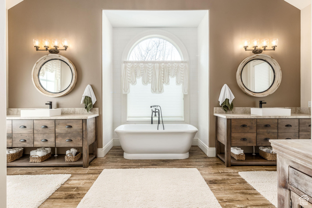 Bathroom featuring dual vanity, hardwood / wood-style flooring, and a bath to relax in