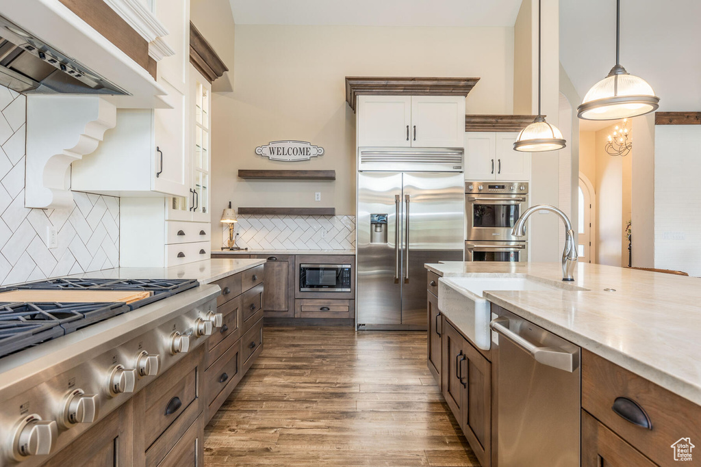 Kitchen with built in appliances, dark hardwood / wood-style floors, tasteful backsplash, and white cabinetry