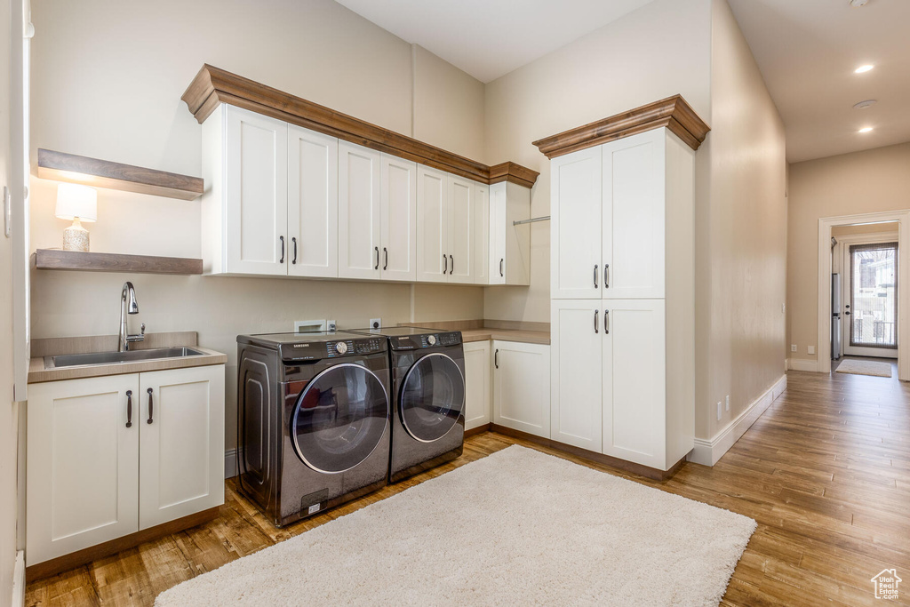 Laundry area featuring independent washer and dryer, sink, hookup for a washing machine, light hardwood / wood-style floors, and cabinets