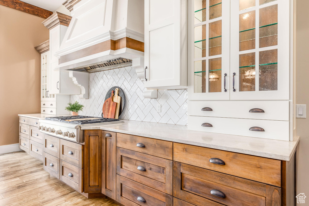 Kitchen with light stone counters, white cabinets, backsplash, custom exhaust hood, and light wood-type flooring