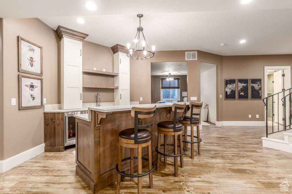 Kitchen featuring a chandelier, a center island, white cabinets, hanging light fixtures, and light wood-type flooring