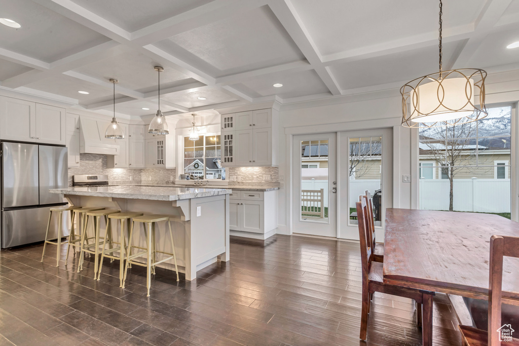 Kitchen featuring coffered ceiling, pendant lighting, white cabinets, backsplash, and stainless steel refrigerator