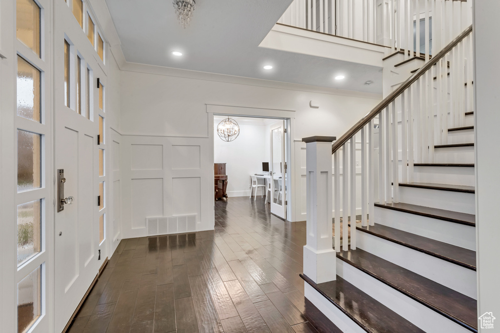 Foyer entrance featuring crown molding, a notable chandelier, and dark wood-type flooring