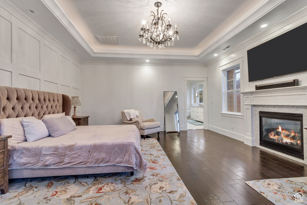 Bedroom with a notable chandelier, ensuite bath, a tray ceiling, and dark wood-type flooring