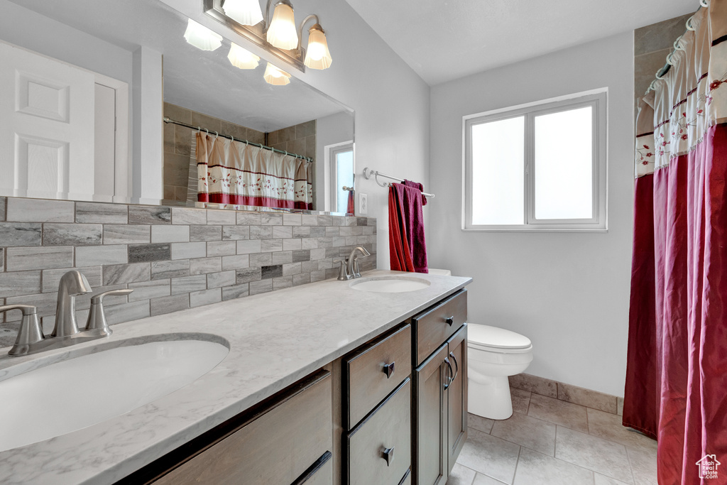 Bathroom with tasteful backsplash, tile floors, double vanity, and toilet